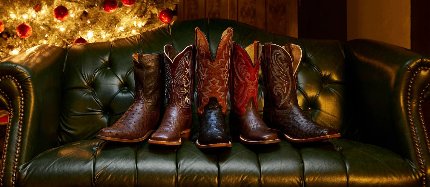 A row of Tony Lama boots on a green leather couch with a glowing Christmas tree in the background.